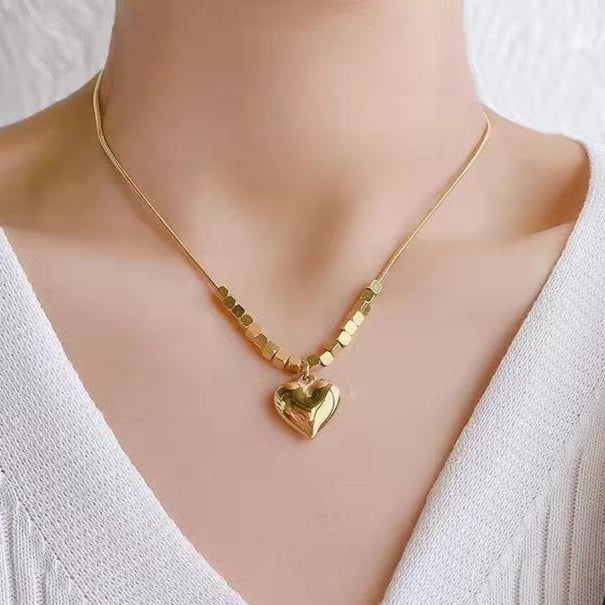 Gold necklace with heart pendant on a model wearing a white sweater.
