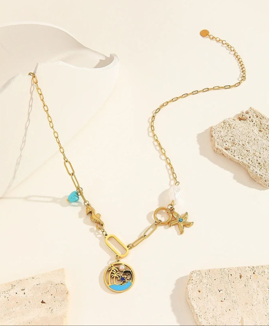 Gold necklace with charms on a textured beige surface