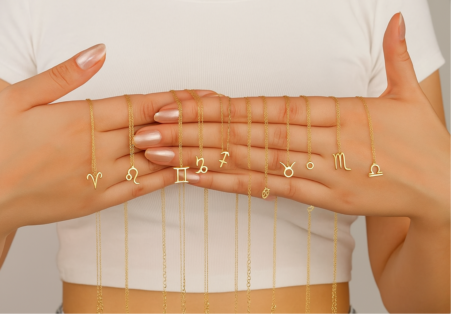 Gold necklaces with zodiac symbols held by hands against a white background